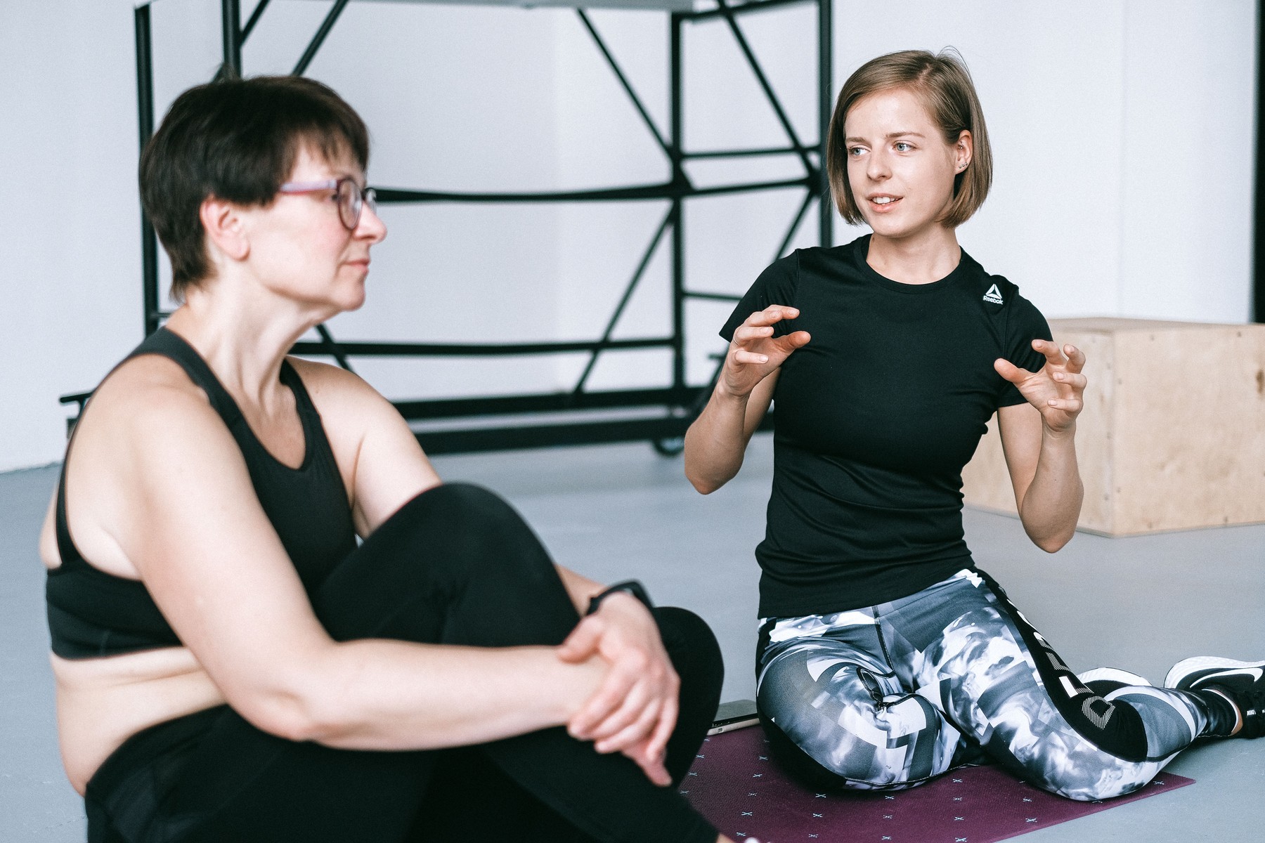 Fitness coach speaking with a prospective member seated on a yoga mat inside a studio