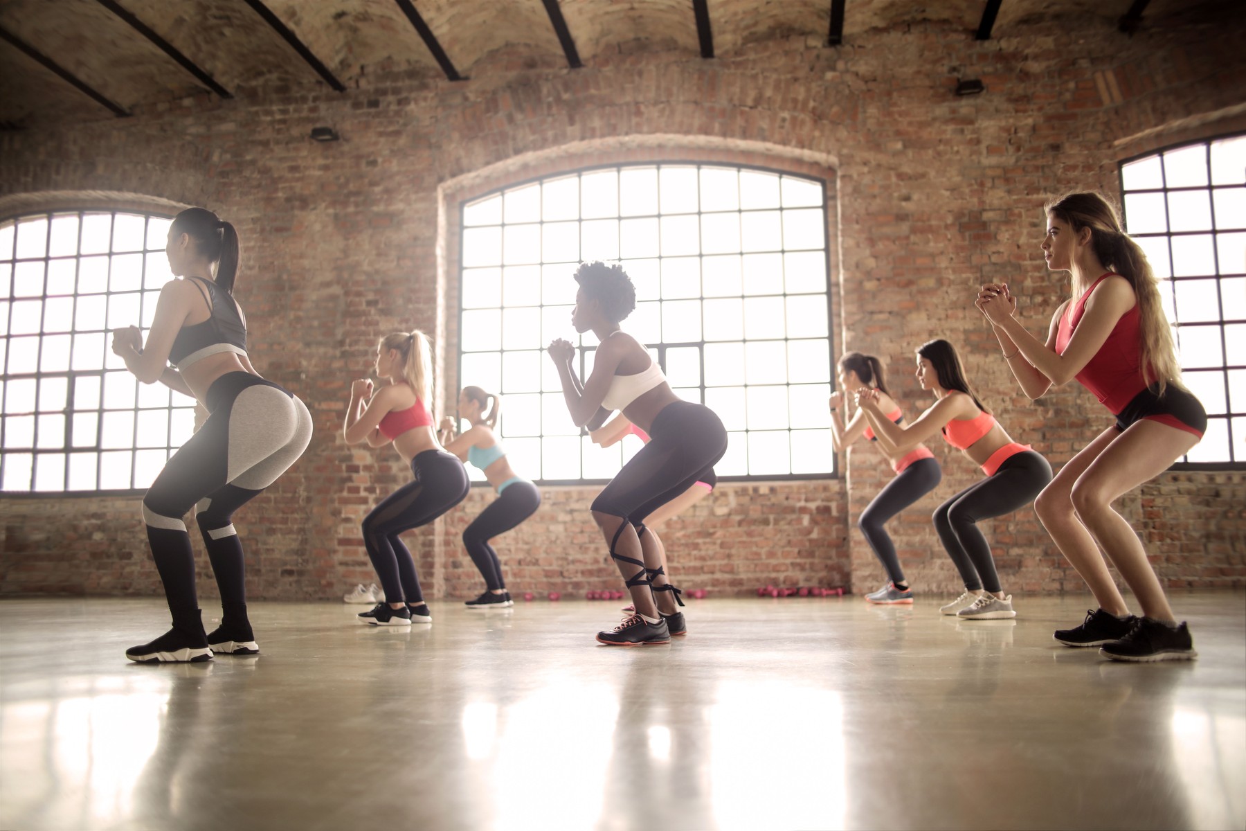 Group of women performing synchronized squats in an industrial-style fitness studio