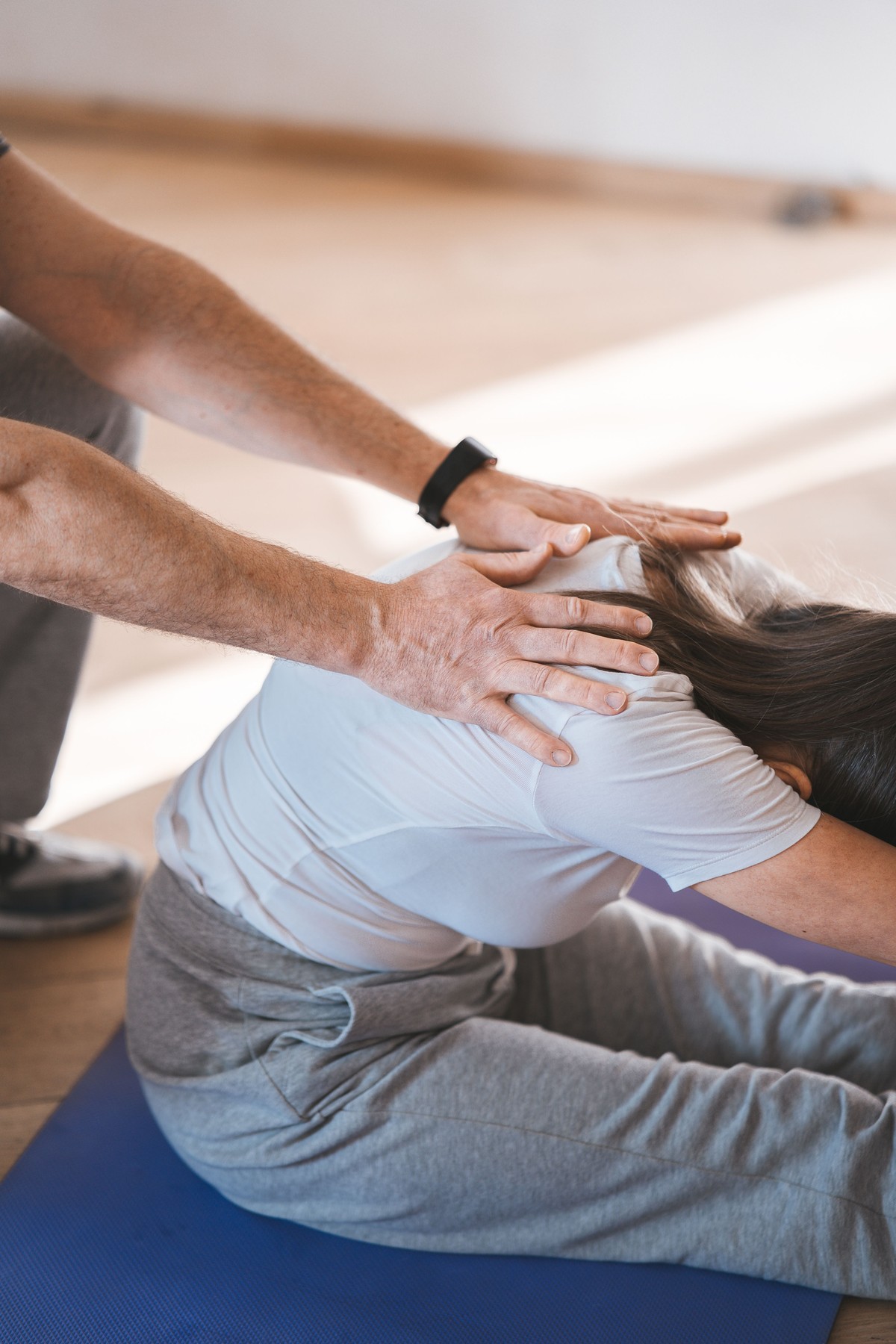 Wellness professional assisting a client with a supported stretch in a bright studio